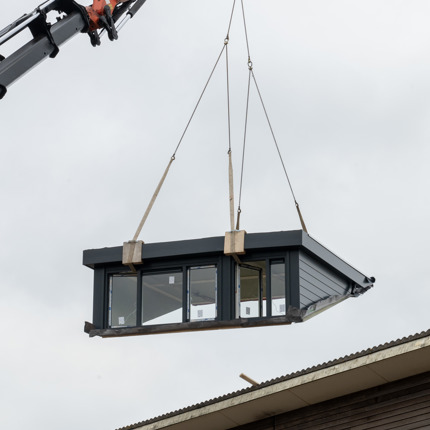 Een dakkapel wordt met een hijskraan geplaatst op het dak van een rijtjeswoning in Vlietestein, Nieuw-Vennep