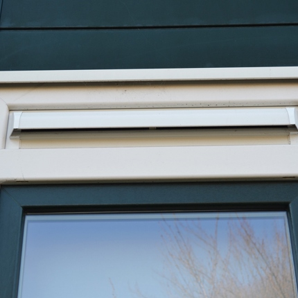 Een ventilatie rooster op een kunststof kozijn